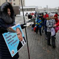 An activist distributes electoral materials in support of presidential candidate President Vladimir Putin in central Moscow on Thursday. The placard reads: \"We are ready to take any challenge of time and win V.V. Putin.\" | REUTERS