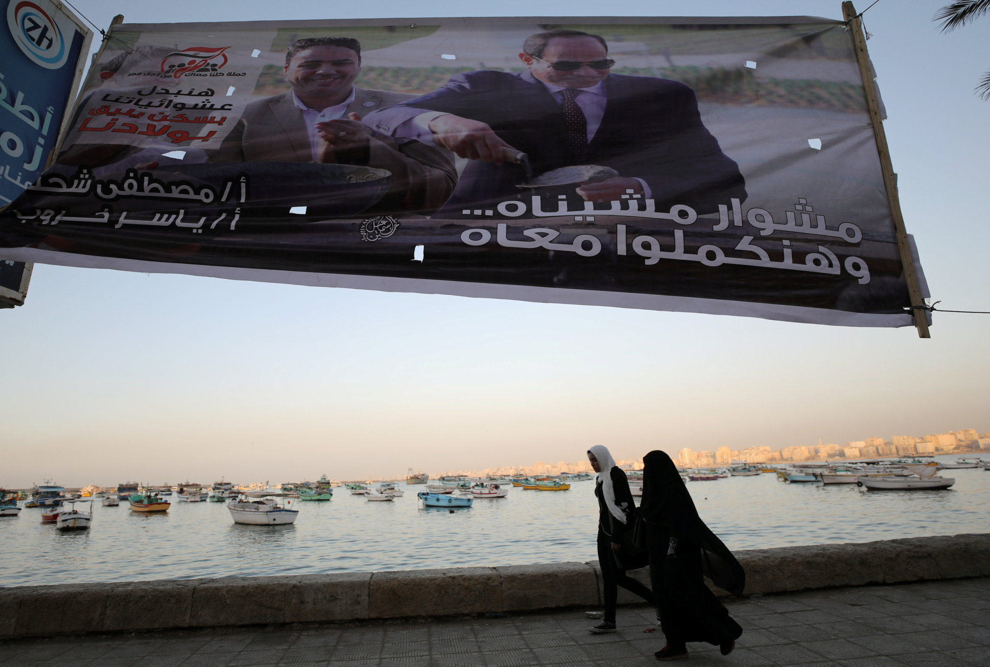 Women walk along the shoreline in front of banners with Egypt's President Abdel Fattah al-Sisi during preparations for the presidential election in Alexandria, Egypt, Sunday. | REUTERS
