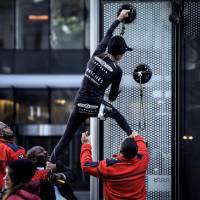 Alain Robert, the French urban climber dubbed Spiderman, is grabbed by security guards preventing him to climb a building hosting the headquarters of French energy giant Engie at La Defense business area, in Paris on Wednesday. | AFP-JIJI