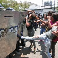 A woman kicks at a riot police shield as relatives of prisoners wait to hear news about their family members imprisoned at a police station where a riot broke out, in Valencia, Venezuela, Wednesday. | AP