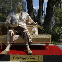 A dog named \"Sassi\" sits next to a golden statue of a bathrobe-clad Harvey Weinstein, seated atop a couch on the sidewalk along Hollywood Blvd., in Los Angeles Thursday. The piece, titled \"Casting Couch,\" is a collaborative effort between a Los Angeles street artist known as Plastic Jesus and Joshua \"Ginger\" Monroe, creator of the nude Donald Trump statue. Plastic Jesus said the piece was meant to shine a light on the entertainment industry\'s sexual misconduct crisis and the disgraced movie mogul\'s prominent role in it. | AP
