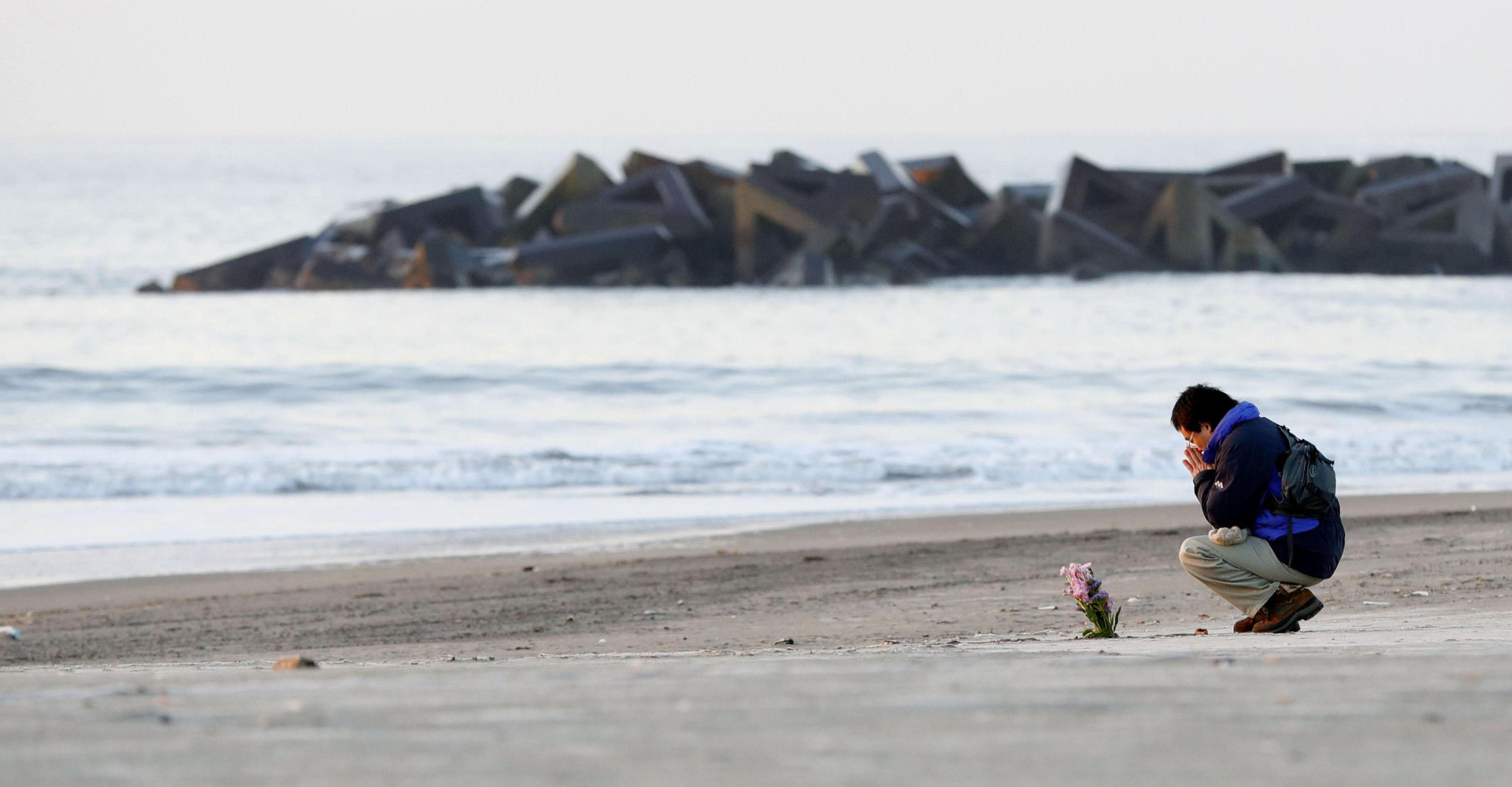 An unidentified man offers prayers and a bouquet on Arahama Beach in Sendai's Wakabayashi Ward early Sunday morning as Japan observed the seventh anniversary of the Great East Japan Earthquake. | KYODO