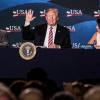 U.S. President Donald Trump waves while sitting next to Maximo Alvarez (left), president of Sunshine Gasoline Distributors, and Irina Vilarino, owner of Las Vegas Cuban Cuisine, during roundtable discussion on tax cuts for Florida small businesses in Hialeah, Florida, Monday. Trump accused China and Russia of devaluing their currencies, breaking from his own Treasury chief\'s view that no major trading partners are currency manipulators. | BLOOMBERG