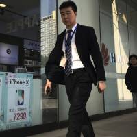 Chinese people walk by a mobile phone accessories shop selling Apple iPhone and Huawei smartphones in Beijing April 20. As trade disputes simmer, Chinese telecommunications giant Huawei, the No. 3 smartphone brand, is shifting its growth efforts toward Europe and Asia in the face of mounting obstacles in the U.S. market. | AP