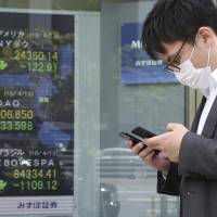 A man walks by an electronic stock board at a securities firm in Tokyo on Monday. | AP