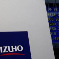 Mizuho Financial Group\'s logo is seen next to an electronic board showing stock price indexes at a branch of Mizuho Securities in Tokyo last year. | REUTERS