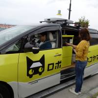 A woman gets a delivery via a self-driving vehicle during an experiment by Yamato Transport Co. and DeNA Co. in Fujisawa, Kanagawa Prefecture, on Tuesday. | KAZUAKI NAGATA