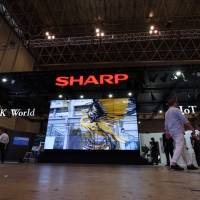 Attendees walk past the Sharp Corp. booth at the CEATEC Japan 2017 exhibition in Chiba Prefecture in October 2017. | BLOOMBERG