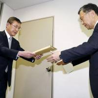 Subaru Corp. President Yasuyuki Yoshinaga (left) submits a report on the scandal-hit automaker\'s data-manipulation confession to an official at the transport ministry on Friday. | KYODO