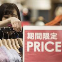 A shopper looks at sweaters at an Ito Yokado outlet in Tokyo. The government will examine steps to mitigate the impact of a consumption tax hike next year. | BLOOMBERG