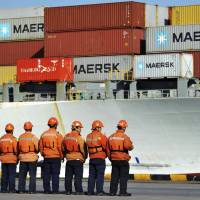 Chinese workers stand in front of a loaded cargo ship docked at a port in Qingdao in east China\'s Shandong province Sunday. Amid falling markets, President Donald Trump\'s new economic adviser, Larry Kudlow, says there is no trade war between the U.S. and China. Another administration official, Treasury Secretary Steve Mnuchin, takes a different tack, saying he\'s \"cautiously optimistic\" that before any threatened tariffs go into place the two nations will reach an agreement. | CHINATOPIX / VIA AP