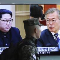 A South Korean marine passes a TV screen showing file footage of North Korean leader Kim Jong Un, left, and South Korean President Moon Jae-in during a news program at the Seoul Railway Station in Seoul, South Korea, on April 18, 2018. North and South Korea have agreed to allow live television broadcasts for parts of a summit between the two leaders scheduled for next week. | AP