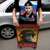 Serbian protester wearing a T-shirt showing Russian President Vladimir Putin holds an anti-NATO poster during a demonstration against Western airstrikes on the Syrian regime, in Belgrade on Sunday. | AFP-JIJI