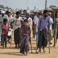 Wounded Rohingya refugees walk with the help of crutches as they await the arrival of a U.N. Security Council team at the Kutupalong Rohingya refugee camp in Kutupalong, Bangladesh, Sunday. | AP