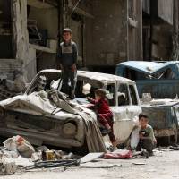 Syrian boys play on a destroyed car in the former rebel-held Syrian town of Douma on the outskirts of Damascus on Thursday, five days after the Syrian army declared that all anti-regime forces have left eastern Ghouta, following a blistering two month offensive on the rebel enclave. | AFP-JIJI