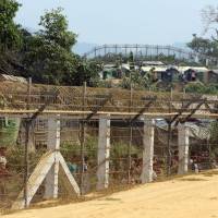 Rohingya people who fled from their towns after the violence in the state of Rakhine, are seen behind a fence on the border line outside Maungdaw, Myanmar, Saturday. | REUTERS