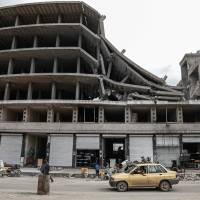 A general view taken Thusday shows a car driving past a damaged building in the northern Syrian enclave of Afrin that Ankara-backed forces captured from Kurdish fighters in recent months. Tens of thousands of people were displaced by the Turkish-led assault on the Afrin region, whose small towns and villages were home to mostly Syrian Kurds. | AFP-JIJI
