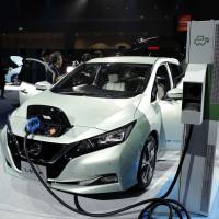 A Nissan Leaf is connected to a charging station during a promotional event in Chiba last September. The idea of using the batteries inside electric vehicles as storage for the entire public power grid is gaining momentum. | BLOOMBERG