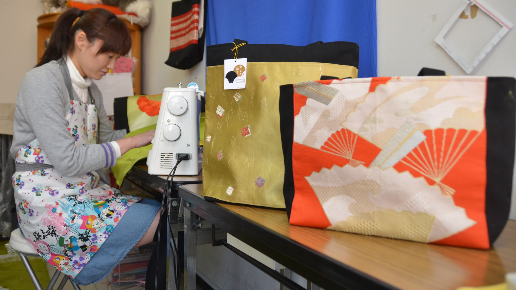 A woman at an establishment that employs people with disabilities in Nagoya uses a sewing machine to create a bag from a distinctively patterned Nagoya obi. | CHUNICHI SHIMBUN