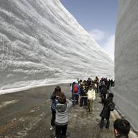 After the road was dug out from under the snow, tourists walk between the high snow walls at Murodo in Toyama Prefecture, on Monday, when the Tateyama Kurobe Alpine Route opened for the season. | KYODO