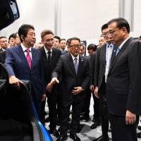 Chinese Premier Li Keqiang listens to Toyota Motor Corp. President Akio Toyoda as Prime Minister Shinzo Abe looks on, during their visit to a Toyota plant in Tomakomai, Hokkaido, on Friday. | POOL / VIA REUTERS