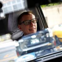 Austrian Wolfgang Loeger, a taxi driver for Hinomaru Kotsu Co., glances in his rearview mirror as he drives a JPN Taxi car, developed by Toyota Motor Co., in Tokyo on May 14. | REUTERS