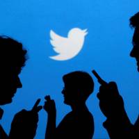 People holding mobile phones are silhouetted against a backdrop projected with the Twitter logo in this illustration picture taken in Warsaw in 2013. | REUTERS