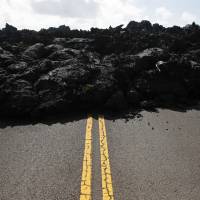 Center lane lines are partially visible along the lava-covered road in the Leilani Estates subdivision near Pahoa, Hawaii, on Friday. Kilauea has destroyed more than 35 structures since it began releasing lava from vents about 40 kilometers east of the summit crater. | AP