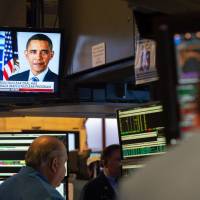 U.S. President Donald Trump and former President Barack Obama potraits are on television as traders work on the floor at the closing bell of the Dow Industrial Average at the New York Stock Exchange on Tuesday in New York. Wall Street stocks finished essentially flat Tuesday as investors tried to assess the potential fallout from Trump\'s decision to pull the U.S. out of the Iran nuclear accord. | AFP-JIJI