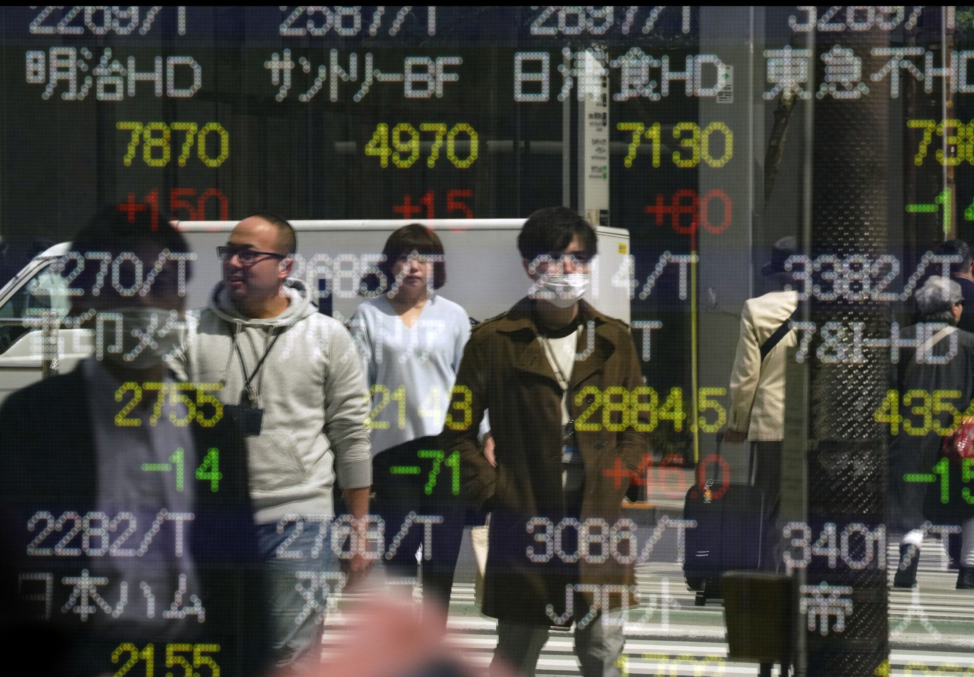 People's reflections are shown in a Tokyo stock indicator. Japan's economy is performing well and deserves more attention as a model of capitalism that manages to balance income growth and income distribution. | AP