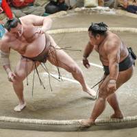 Yokozuna Hakuho (left) keeps his balance and defeats No. 2 maegashira Shohozan in their Summer Grand Sumo Tournament match on Tuesday at Ryogoku Kokugikan. | KYODO