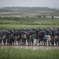 Rohingya Muslim refugees wait in line under the rain during a food distribution under at Nayapara refugee camp in Bangladesh\'s Ukhia district last October. The first monsoon rains have hit camps in Bangladesh housing around a million Rohingya refugees, triggering floods and landslides but for now no casualties or major damage, officials said on Sunday. | AFP-JIJI