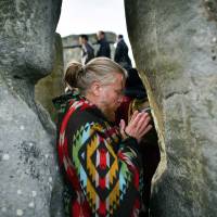 A man gestures between stones as the sun rises through Stonehenge, where crowds of people gather to celebrate the dawn of the longest day in Wiltshire, England, on June 21, 2018. The Neolithic Wiltshire monument is built along the solstice alignment of the summer sunrise and the winter sunset. | AP