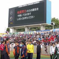 High school students participating in a track and field competition in Maebashi, Gunma Prefecture, on Sunday afternoon look at a board saying that the event has been temporarily suspended following an earthquake. | KYODO