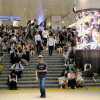 People sit on the stairs of Hankyu Railway\'s Umeda Station in the city of Osaka on Monday morning, after train operations were suspended following a major earthquake that hit the Kansai region. | KYODO