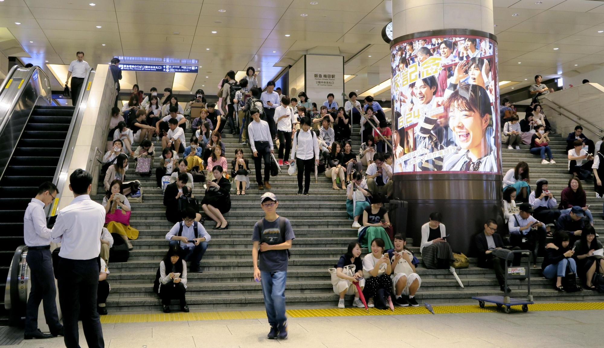 People sit on the stairs of Hankyu Railway's Umeda Station in the city of Osaka on Monday morning, after train operations were suspended following a major earthquake that hit the Kansai region. | KYODO