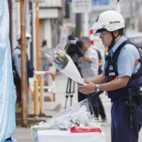 A police officer lays flowers Wednesday on a table set up before a police box in the city of Toyama where a police officer was stabbed to death the day before. The officer\'s gun was also stolen during the attack. | KYODO