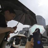Women shade themselves under parasols in the Ginza shopping district in Tokyo on Monday. In the afternoon the temperature hit 41.1 degrees in Kumagaya, Saitama Prefecture, a new record high for Japan. | AP