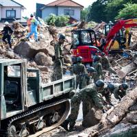 Rescue workers and soldiers clear debris from a street in a flood-hit area in Kumano, Hiroshima Prefecture, on Monday. Torrential rain across western Japan has forced some automakers and other companies to suspend operations. | AFP-JIJI