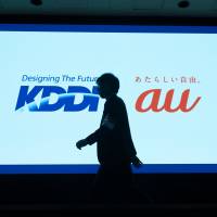 A man walks past the KDDI corporate logo in Tokyo. The phone carrier reportedly plans to end its four-year installment smartphone payment plan after a government watchdog said last month that the contract poses antitrust problems. | BLOOMBERG