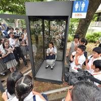 A Showa Elementary School student tries a \"magic mirror toilet\" that simulates the practice of open defecation, at an event held Thursday at Showa Women\'s University. | YOSHIAKI MIURA
