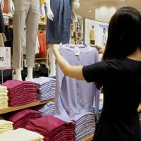 A woman holds up a garment at a Uniqlo store in Ikebukuro, Tokyo, in April. | KYODO