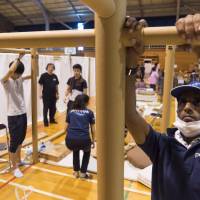 Peace Winds Japan volunteers install cardboard-based structures designed by architect Shigeru Ban at a gym converted into a shelter in Kurashiki, Okayama Prefecture.  | COURTESY OF PEACE WINDS JAPAN