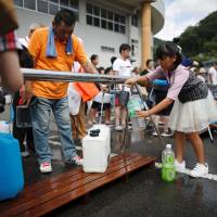 Local residents fill up water containers near a flooded area at Mihara No. 2 junior high school, which was acting as an emergency water supplying station, in Mihara, Hiroshima Prefecture, on Monday. | REUTERS