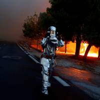 A firefighter wears a flame resistant uniform as a wildfire burns in the town of Rafina, near Athens, Monday. | REUTERS