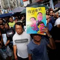 A protester carries a leaflet mocking top officials during a march in Hong Kong on Sunday to mark the 21st anniversary of the city\'s handover to Chinese sovereignty from British rule. | REUTERS
