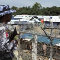 A Myanmar border guard stands guard near a fence at a no-man\'s land between Myanmar and Bangladesh, near Taungpyolatyar village, Maung Daw, northern Rakhine State, Myanmar, Friday. Ten months after a government security operation in Myanmar\'s Rakhine state sparked a humanitarian crisis that sent hundreds of thousands fleeing to neighboring Bangladesh, at least 5,000 Rohingya Muslims are still living in a no man\'s land between the two countries. While Myanmar has built a border fence that prevents them from returning to their villages inside the country, the refugees have decided not to enter Bangladesh. | AP