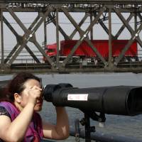 Tourists peer through high-powered binoculars into North Korea in May as a truck crosses the Friendship Bridge connecting China and  North Korea at the Chinese border town of Dandong. | AP