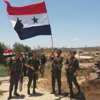 A handout picture released by the official Syrian Arab News Agency (SANA) on Thursday shows Syrian army soldiers carrying the national flag in the village of Hamidiya in the southern province of Quneitra. | SANA / VIA AFP-JIJI