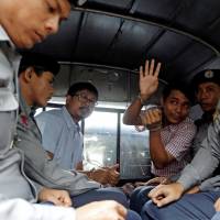Detained Reuters journalists Wa Lone and Kyaw Soe Oo sit beside police officers as they leave Insein court in Yangon, Myanmar, on Monday. | REUTERS